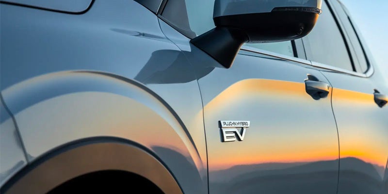 White 2025 Mitsubishi Outlander Hybrid EV emblem at sunset